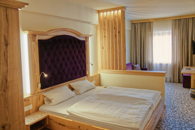 Hotel room »Landhaus exklusiv Provence«, bed and room elements made of oak wood, large, purple, quilted plush headboard behind the bed